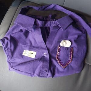 Folded purple shirt with a pen and name tag on a gray surface.