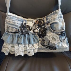 A denim handbag with lace and floral embellishments.