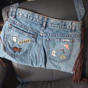 Denim purse made from repurposed jeans with decorative patches and fringe.