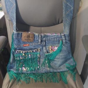 Denim bag with colorful embroidery and fringe detail.